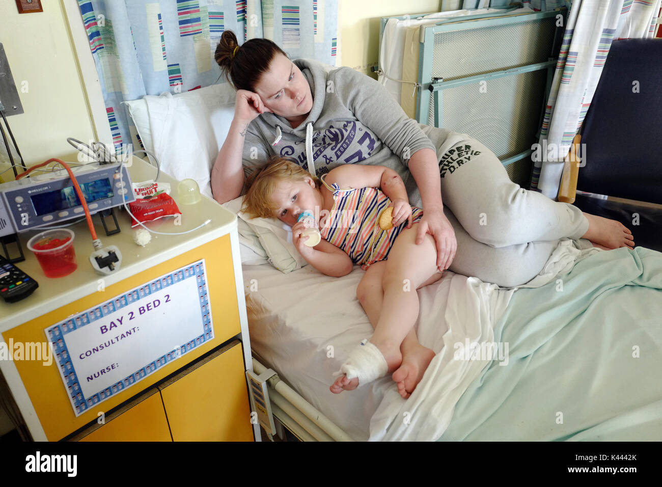 Mother lying with her child in a hospital ward, trying to comfort her. Stock Photo