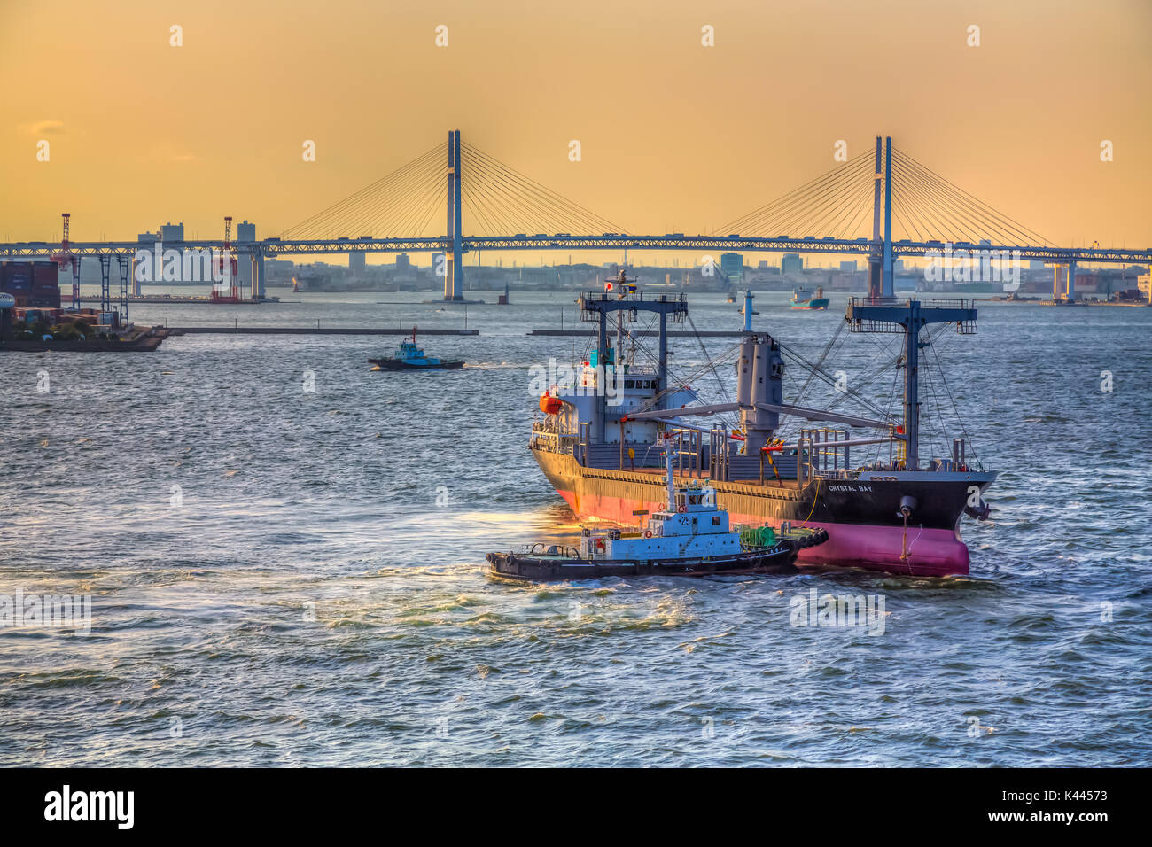 A cargo ship and tugboat with sunset and bridge at the port of Yokohama, Japan, Asia Stock Photo