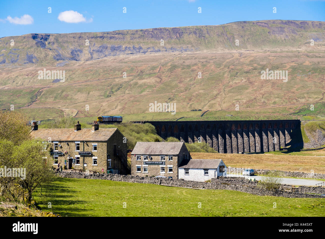 Station Inn pub and Bunk Barn with diesel train crossing Ribblehead viaduct below Whernside. Yorkshire Dales National Park North Yorkshire England UK Stock Photo