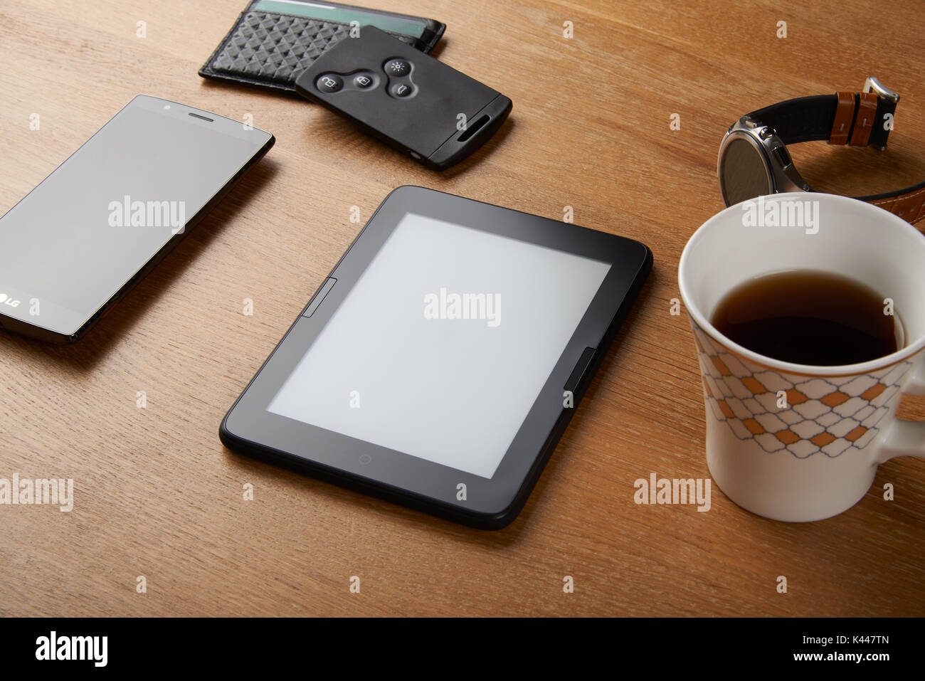 E-book device with Smart key, card wallet, smart watch, smart phone and a cup of coffee on a wooden table. The device is a dedicated device for readin Stock Photo