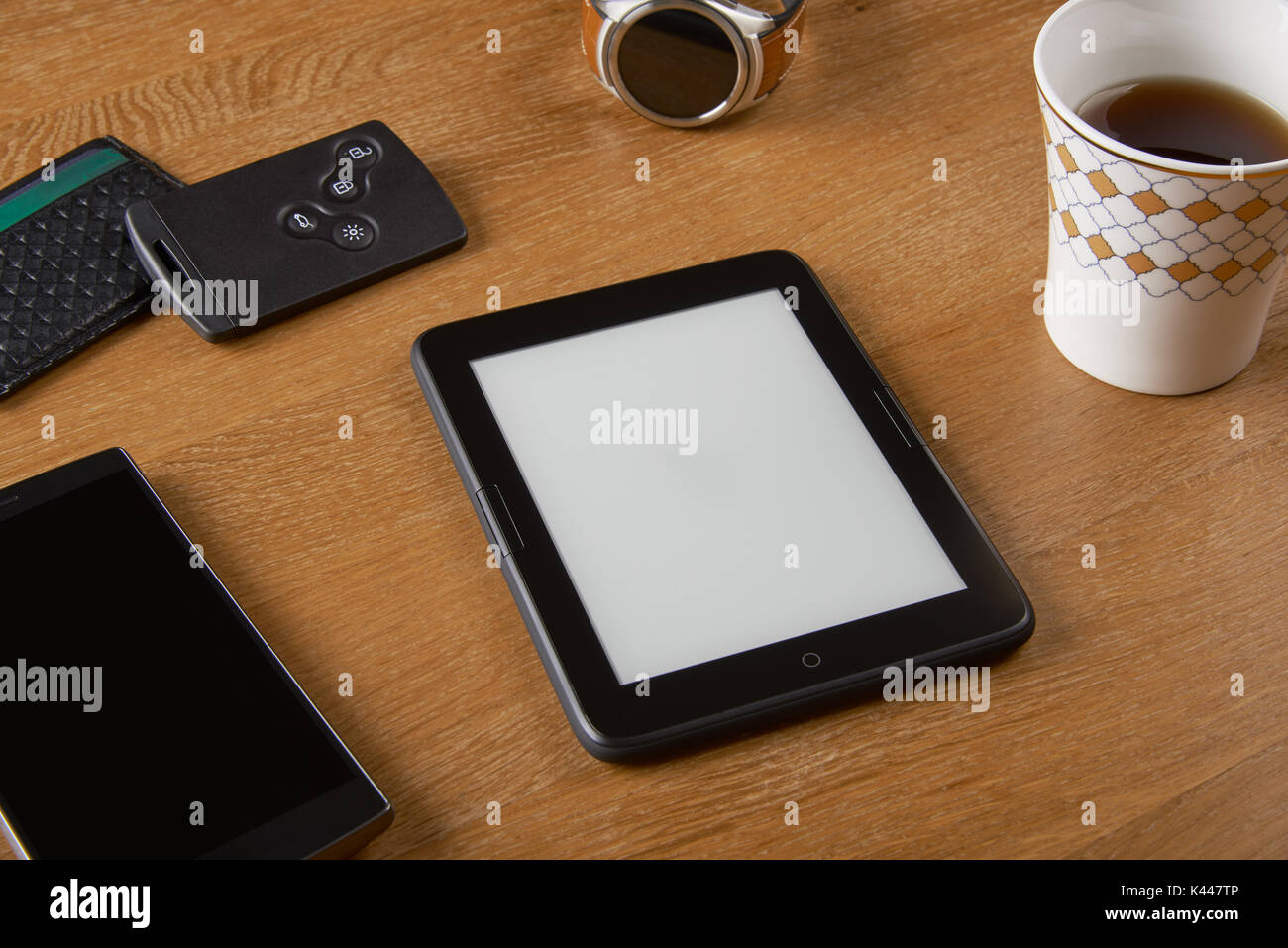 E-book device with Smart key, card wallet, smart watch, smart phone and a cup of coffee on a wooden table. The device is a dedicated device for readin Stock Photo