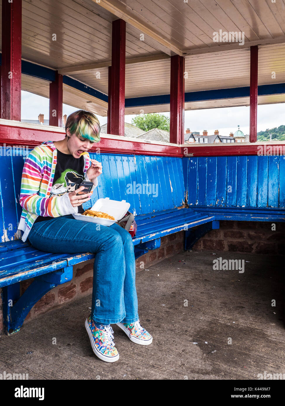 A young girl eats fish and chips in a shelter on the promenade at Minehead in Somerset. Stock Photo