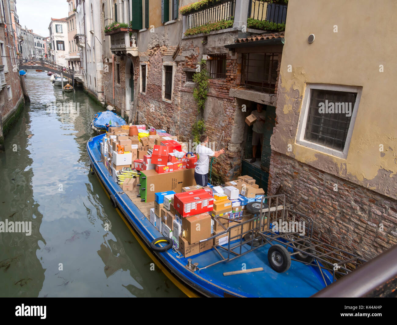 Goods delivery on a Venice canal, Italy. A deliveryman throws boxes to