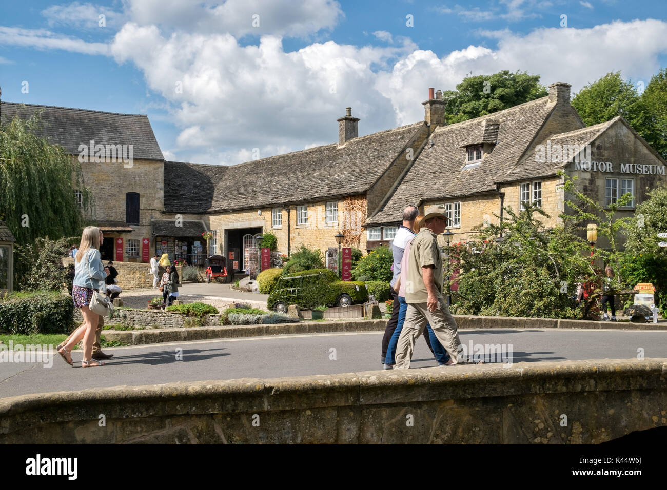 Visitors walking over a bridge crossing the river Windrush infront of the Cotswold motoring museum in Bourton on the Water, Gloucestershire, UK Stock Photo