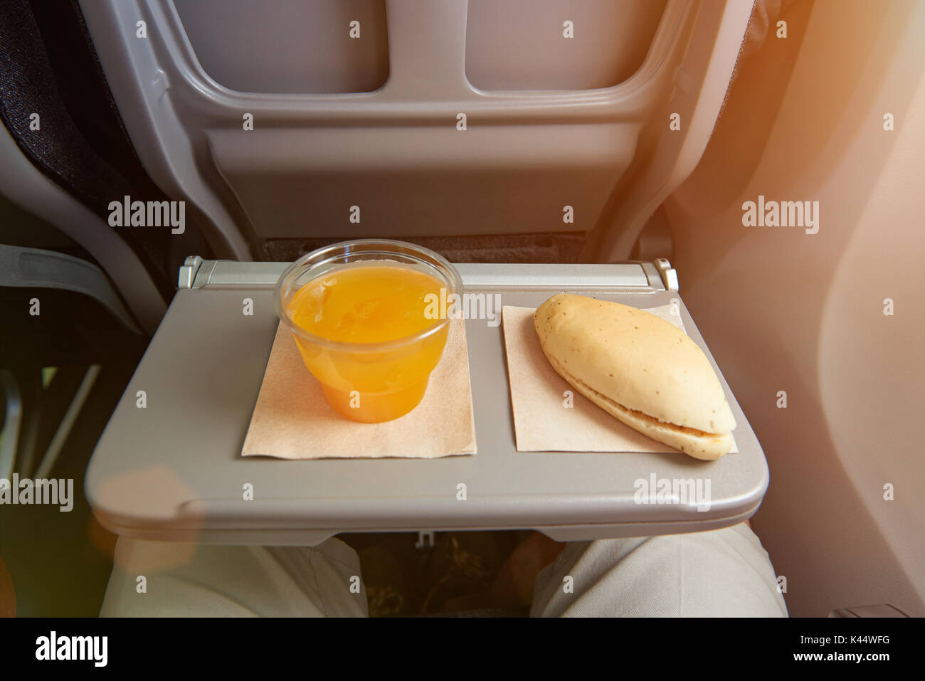 Small meal in airplane back seat table. Cup of orange juice and sandwich Stock Photo