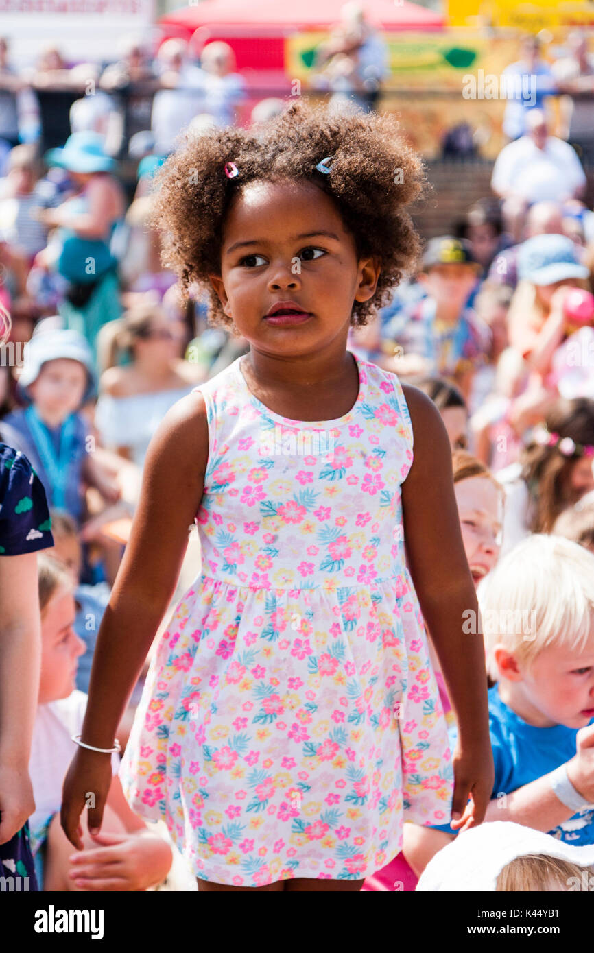 Black child, 5-6 years, standing among crowd of sitting children, eyes looking to the side with very intense cornerned facial expression. Stock Photo