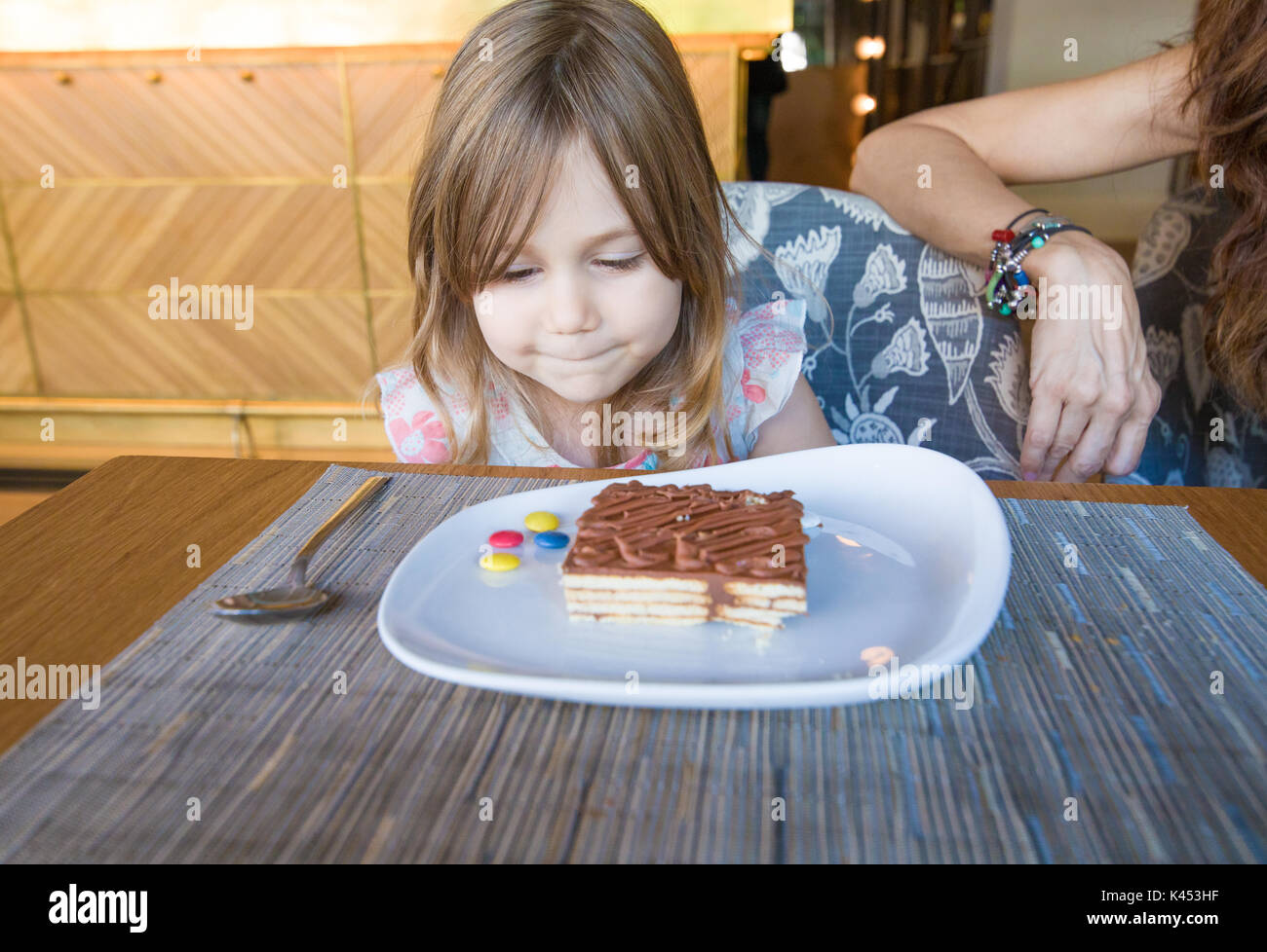 three years old child looking portion of chocolate cake and candy colorful pills in white dish sitting next to woman in restaurant Stock Photo