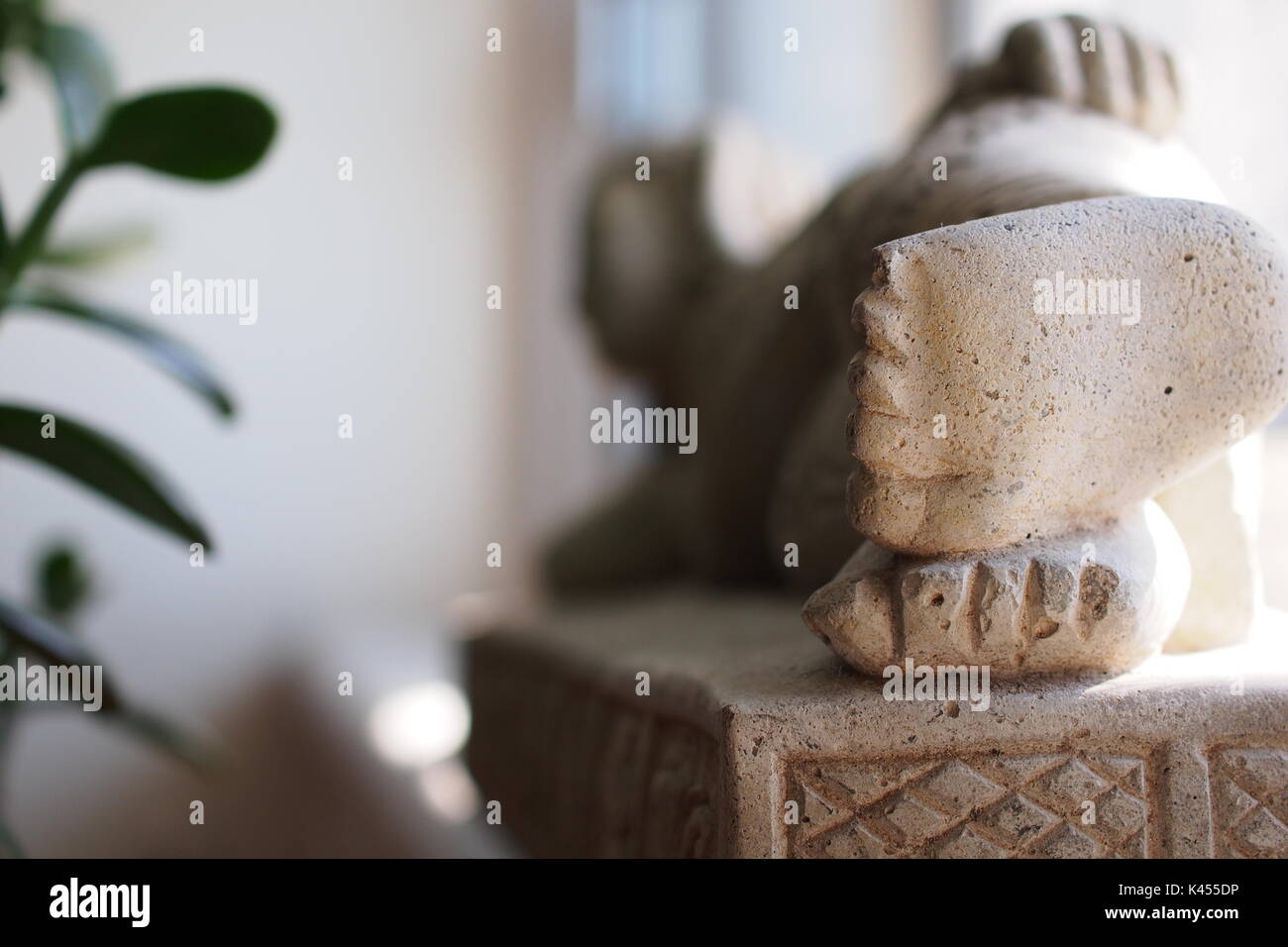 Close up of the feet of a 30cm statue of the reclining buddha on a window sill, facing a jade plant. Stock Photo