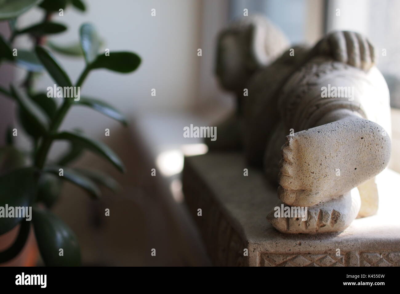 Close up of the feet of a 30cm statue of the reclining buddha on a window sill, facing a jade plant. In Grandma's apartment. Stock Photo