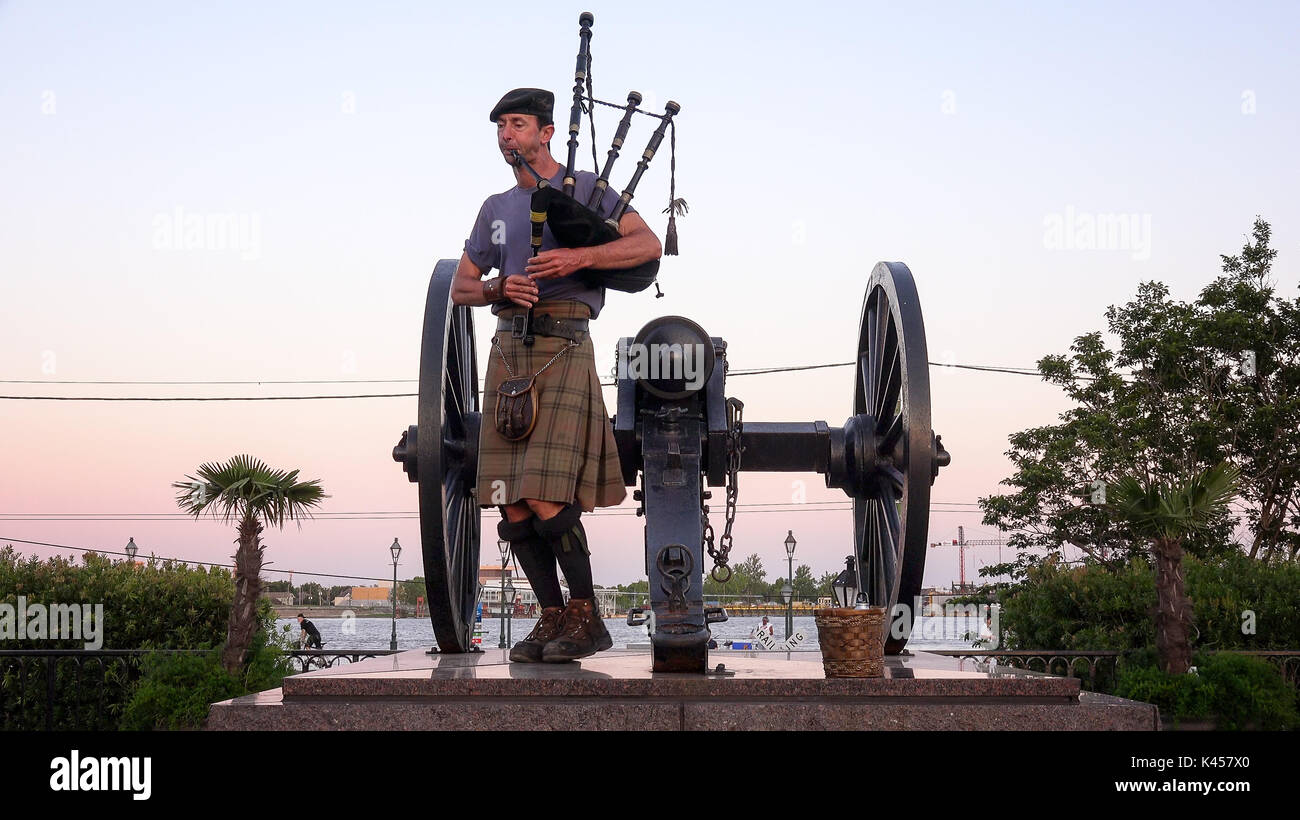 Man in kilt playing bagpipes next to cannon at sunset at Jackson Square in the French Quarter of New Orleans, Louisiana Stock Photo