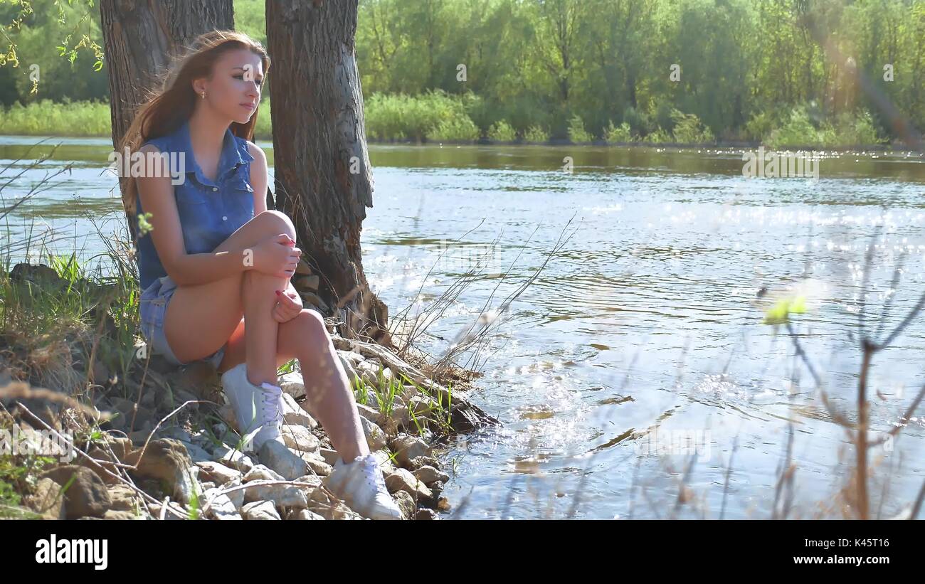 Girl on the river bank. Woman sits by the water nature lifestyle Stock ...