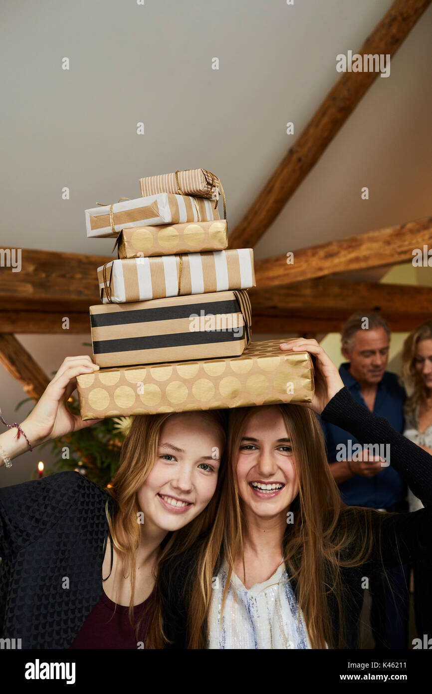 Two girls with presents in front of Christmas tree, cheerful, laughing, parents in background Stock Photo