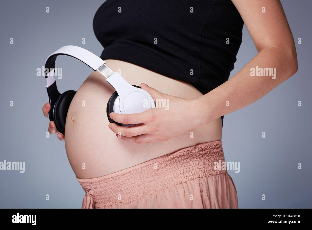 A photo of pregnant woman putting headphones on her belly Stock Photo