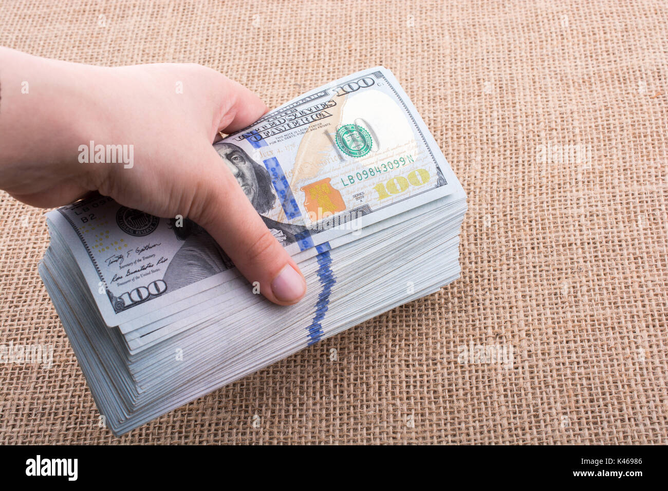 Hand holding banknote bundle of US dollar on a linen canvas background ...