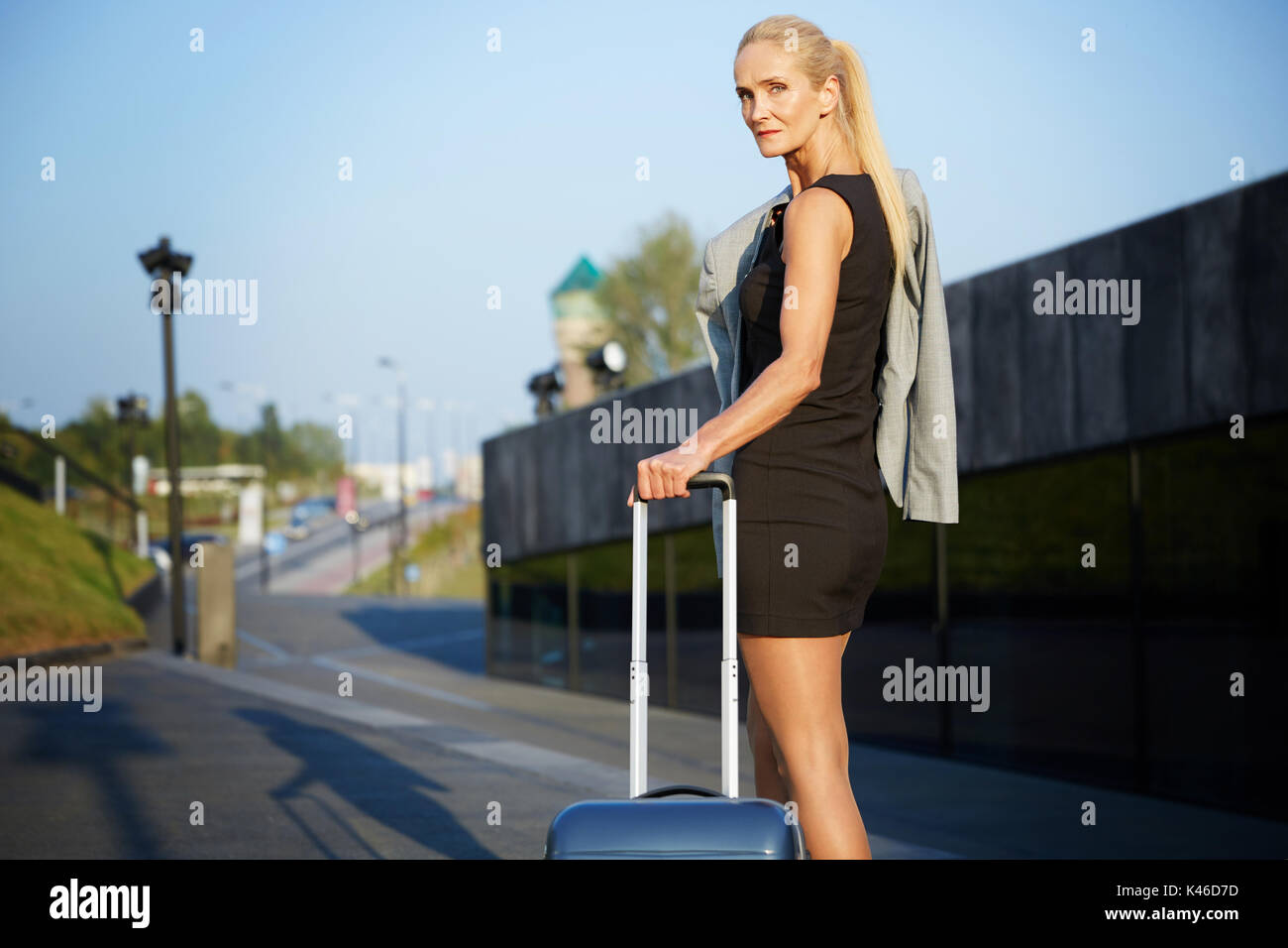 Portrait of mature businesswoman pulling suitcase down the street. Stock Photo