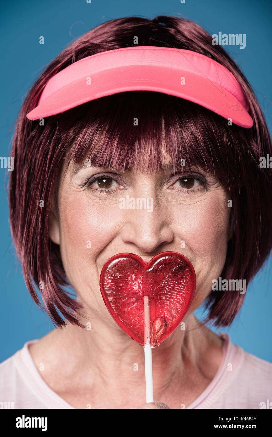 portrait of beautiful elderly woman licking lollipop in form of heart Stock Photo