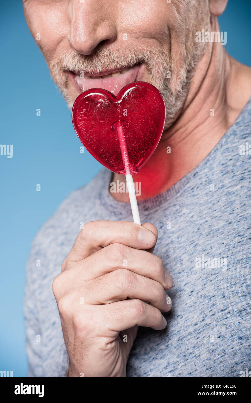 cropped shot of elderly man licking lollipop in form of heart Stock Photo