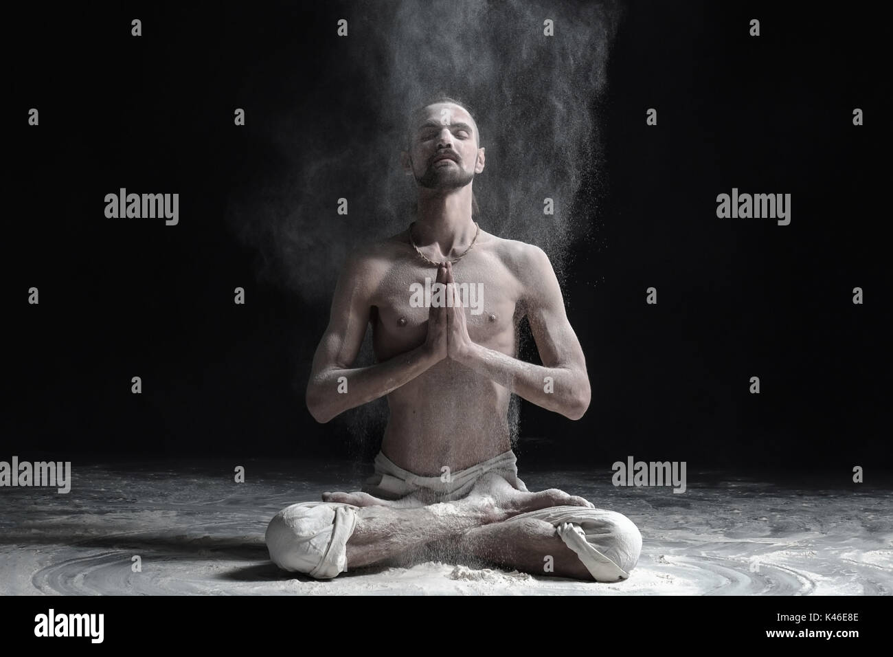 A yoga teacher sits in a sukhasana on a black background. Stock Photo