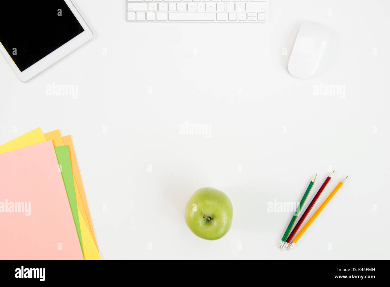 Top view of keyboard, computer mouse, digital tablet with blank screen, green apple and office supplies at workplace Stock Photo