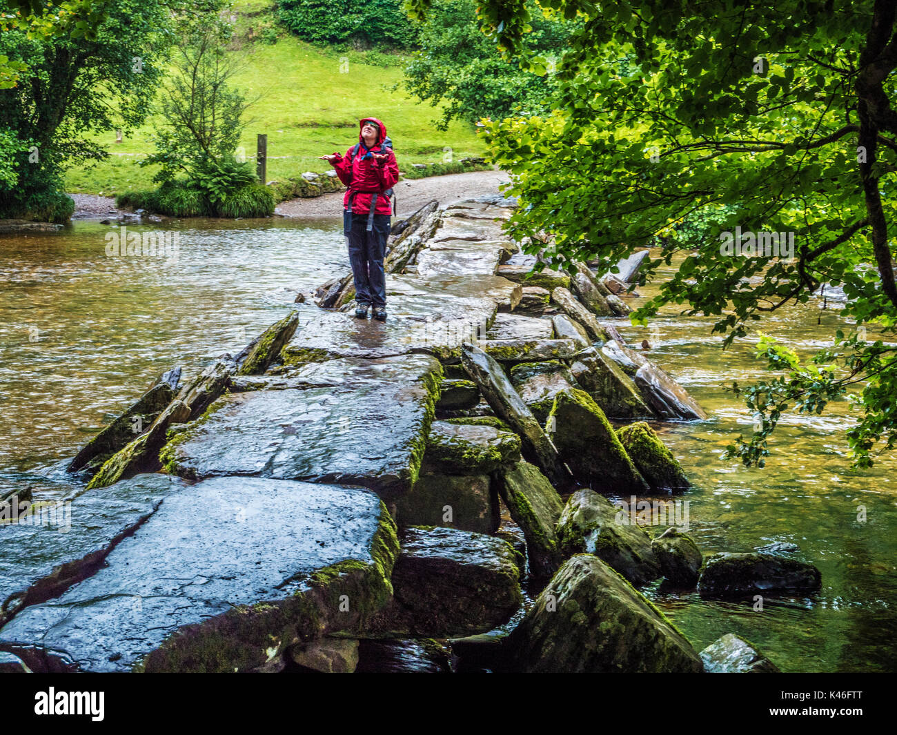 Young girl looks skywards wondering when the rain will stop on Tarr Steps in Exmoor, Somerset. Stock Photo