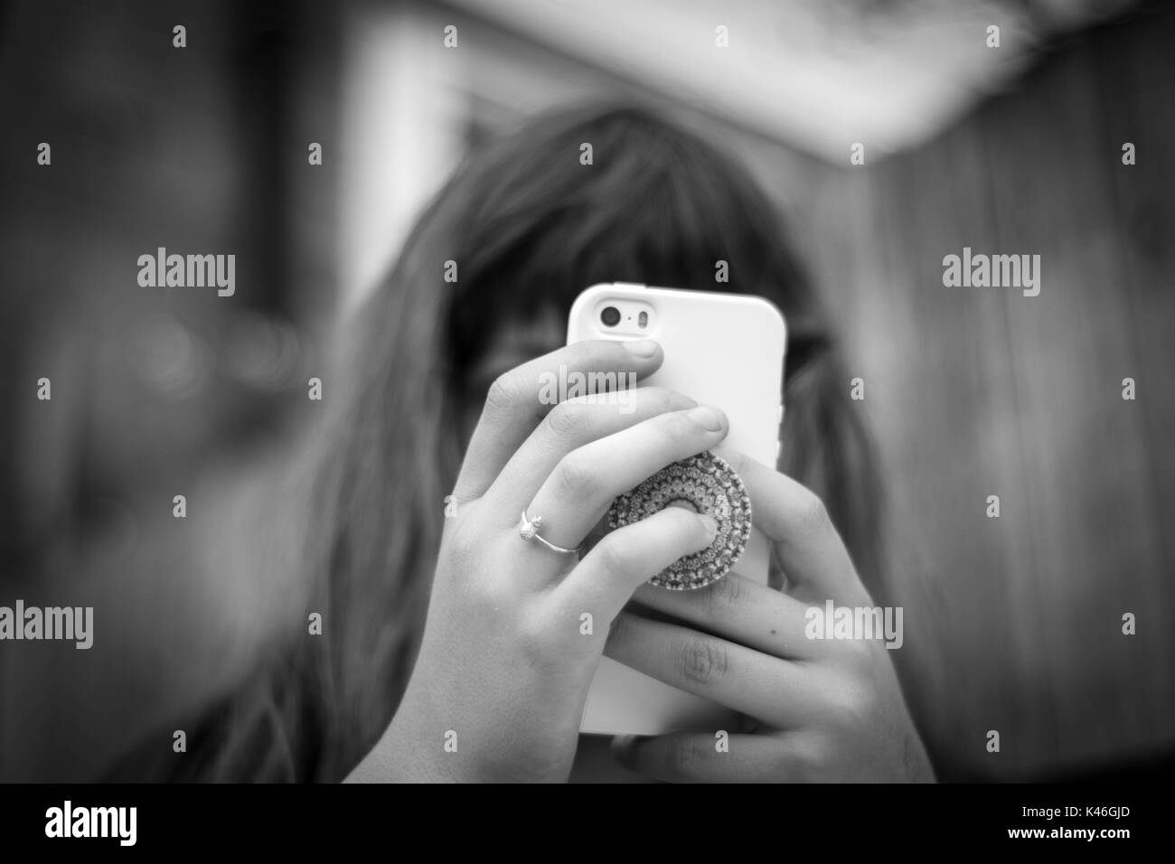 Black & White image of girl holding iPhone with two hands with a blurred background Stock Photo