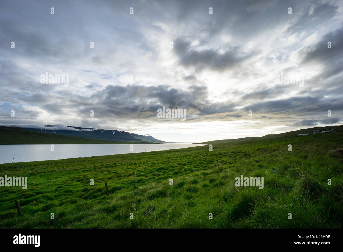 Iceland - Magical cloud formations over lake behind green glowing fields at dawn in summer Stock Photo