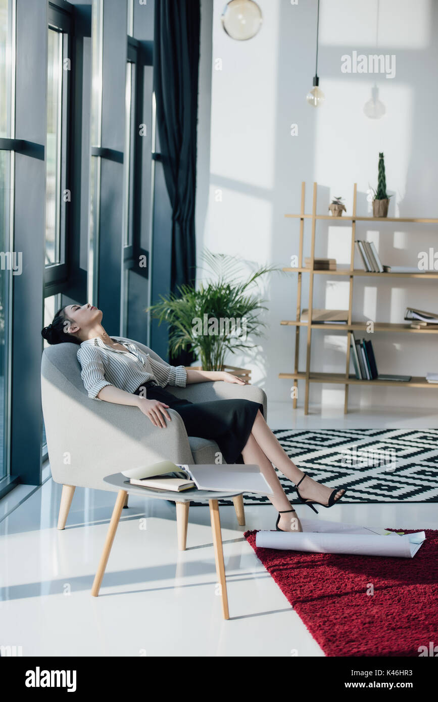 Young tired asian businesswoman sitting in chair with closed eyes Stock Photo