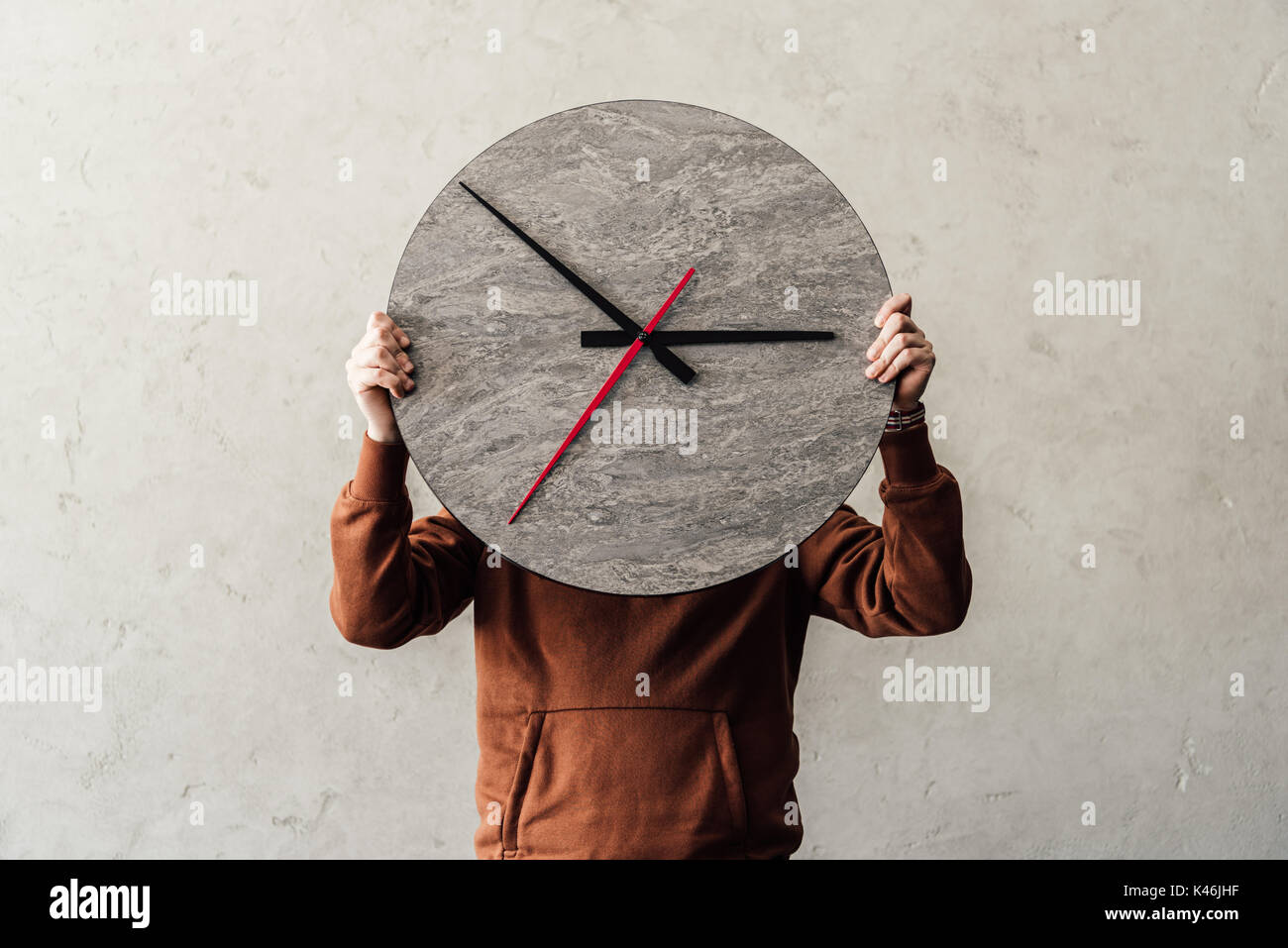 Unrecognizable person covering face with stylish round wooden clock Stock Photo