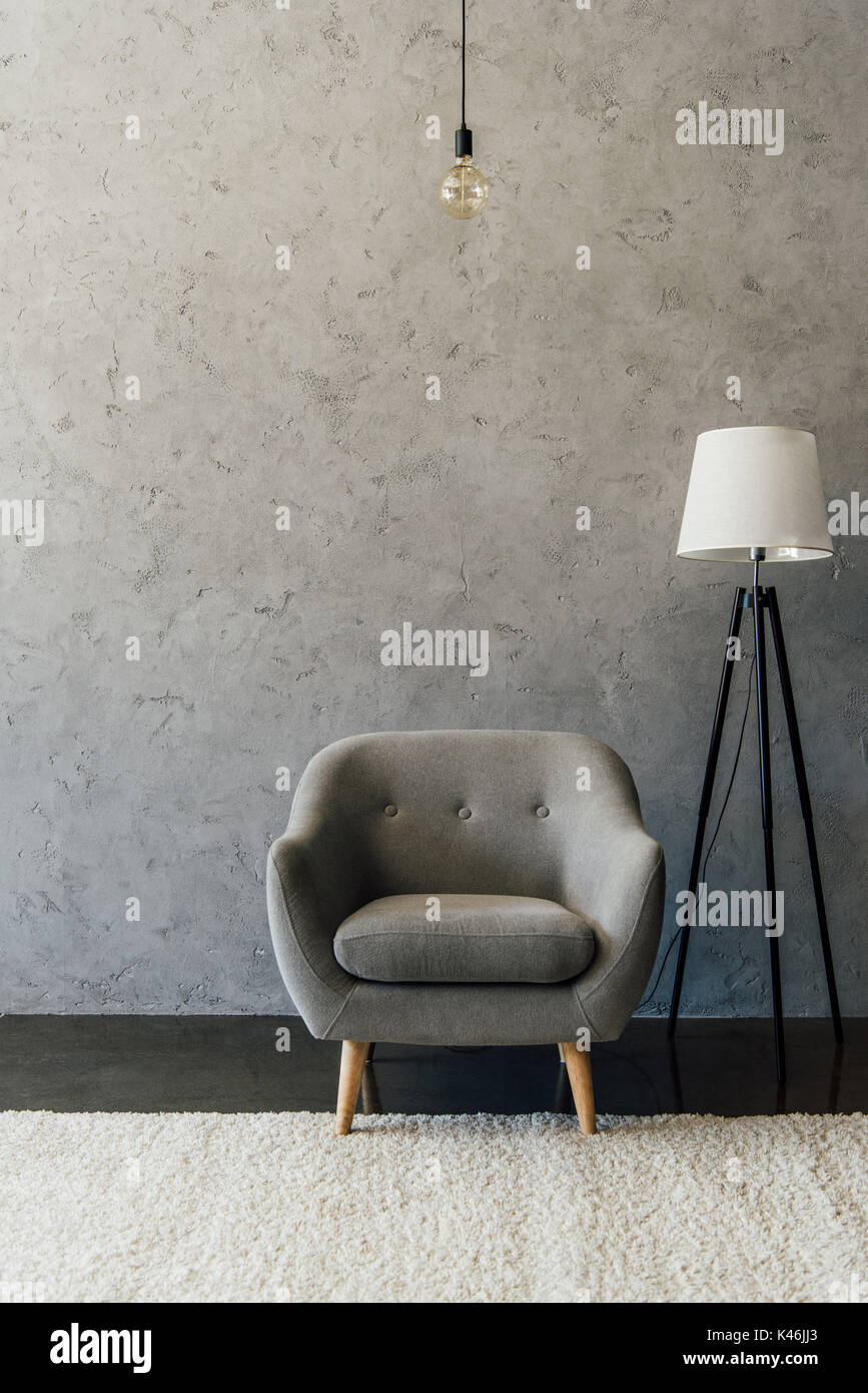 Cozy grey armchair on white carpet and modern lamp in empty room Stock Photo