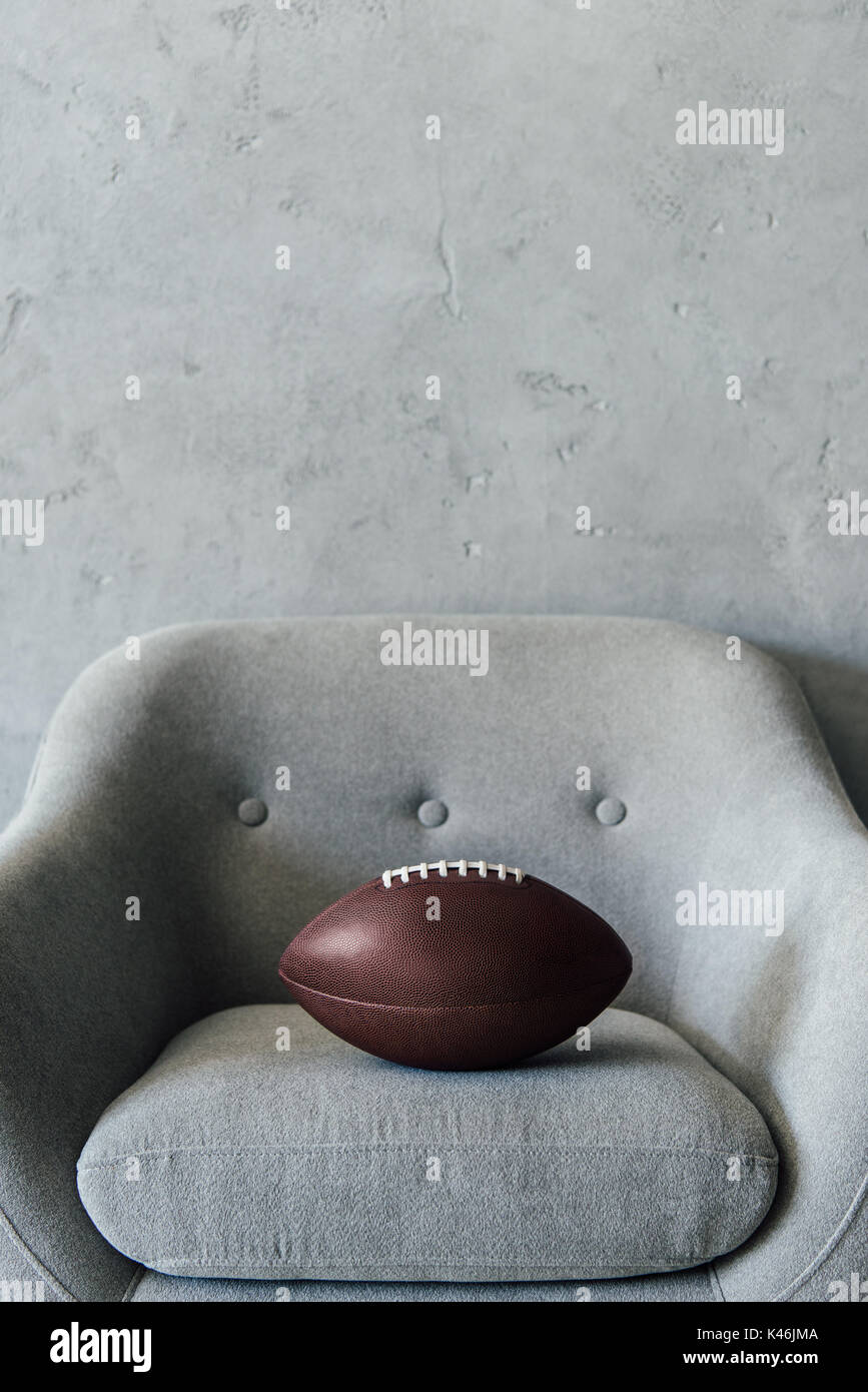 american football ball on grey textile armchair at empty room Stock Photo