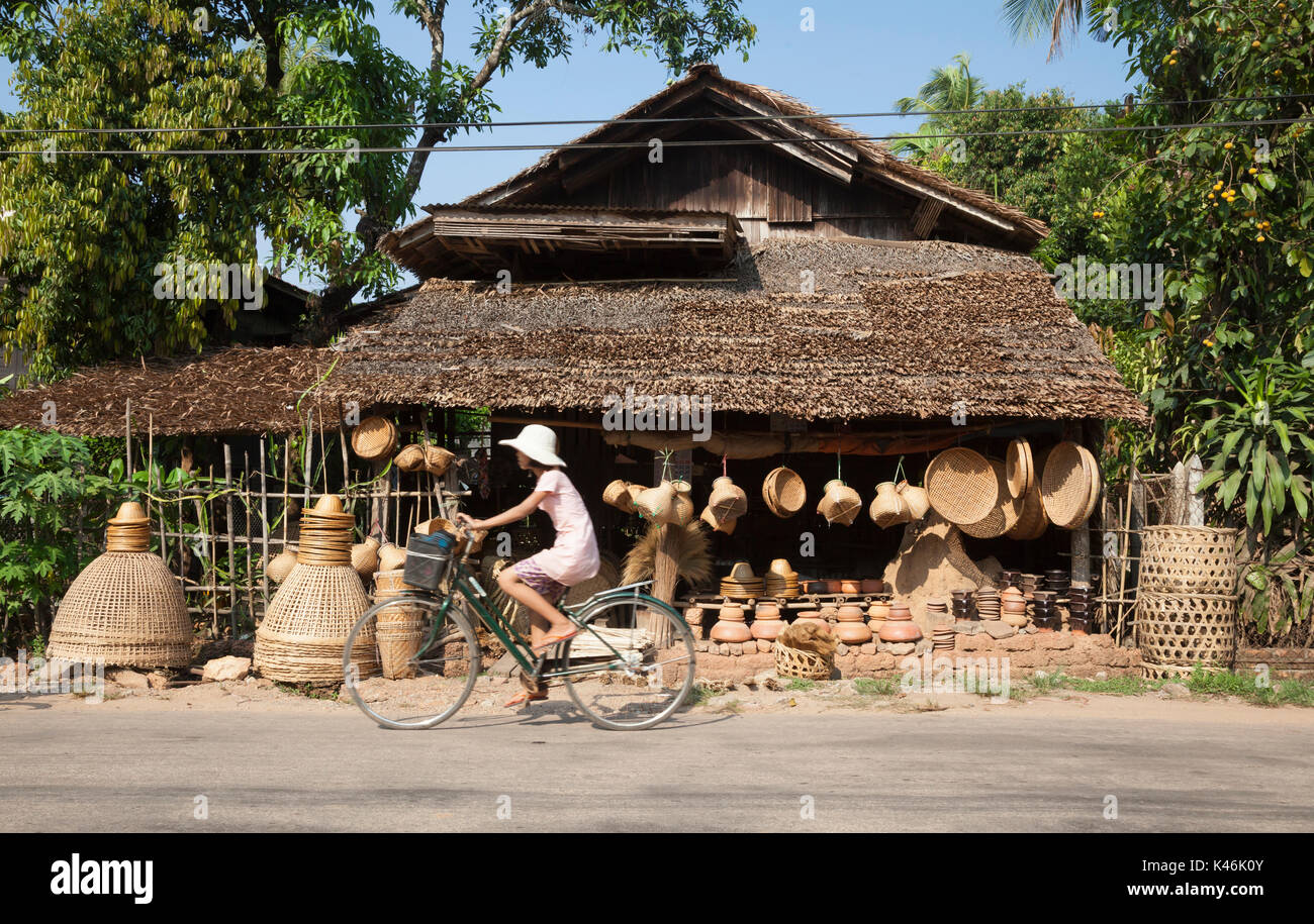 Girl rides past village basket shop in rural Bilugyun, Myanmar Stock Photo