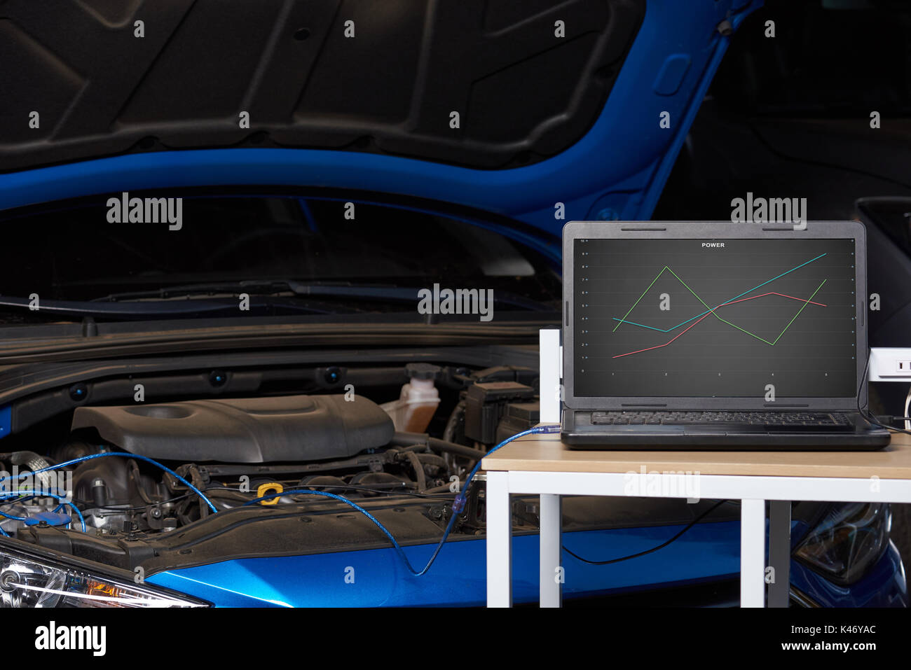 Car engine chip tuning station table with laptop on blue open hood vehicle background Stock Photo