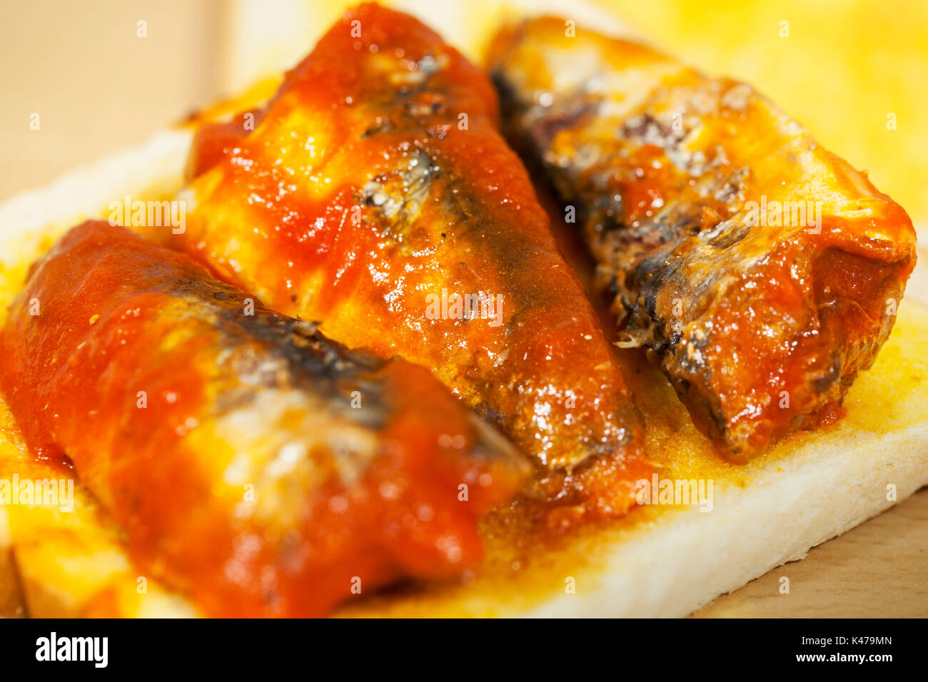 Three sardines topped and tailed in tomato sauce laying on a slice of