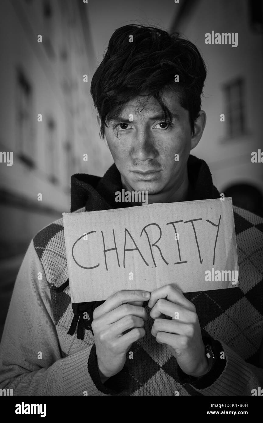 Close up of a homeless with cardboard description of charity, in a blurred background Stock Photo