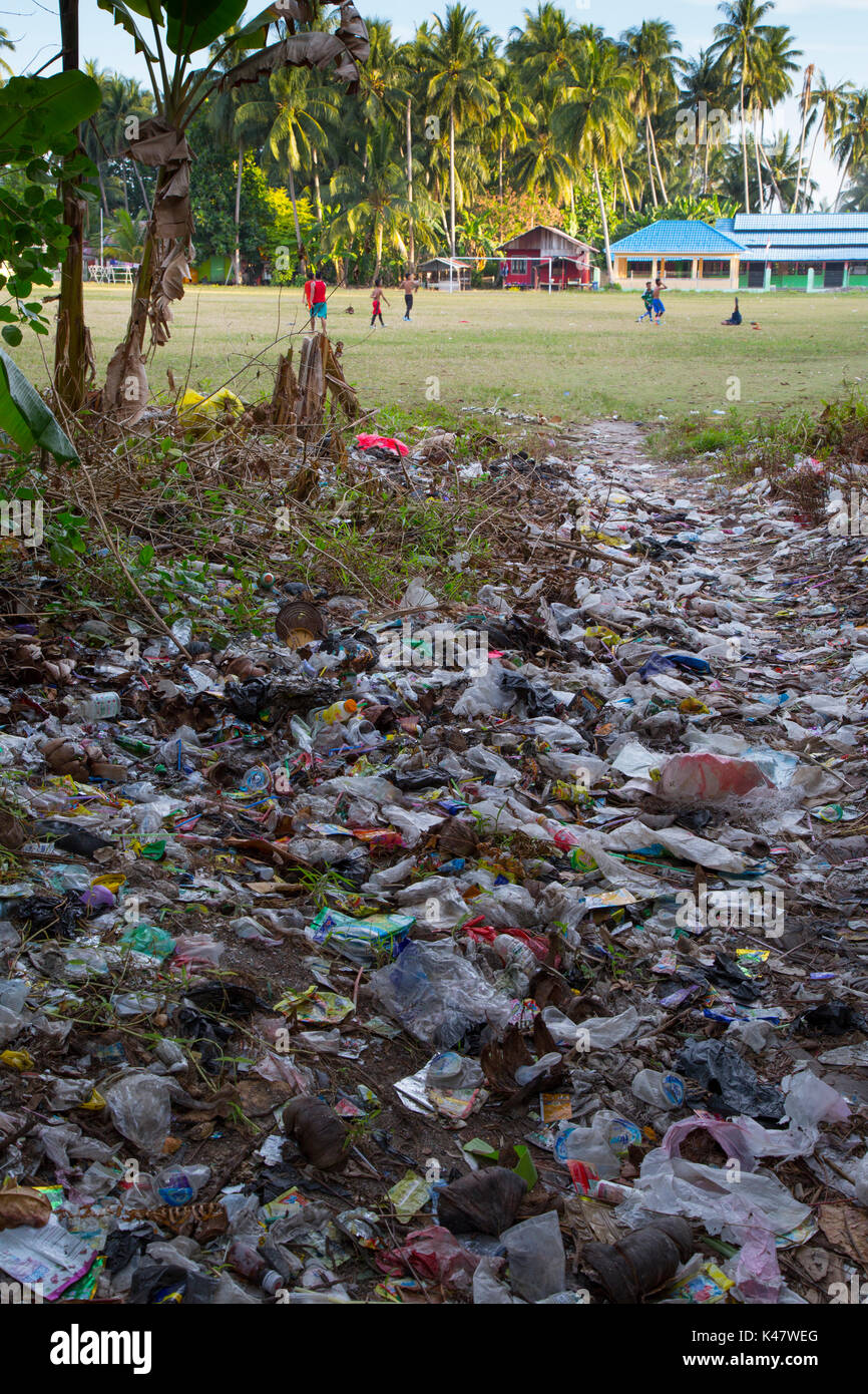 Plastic trash and other garbage lying on ground with children playing football behind at Derawan Island, Kalimantan Stock Photo