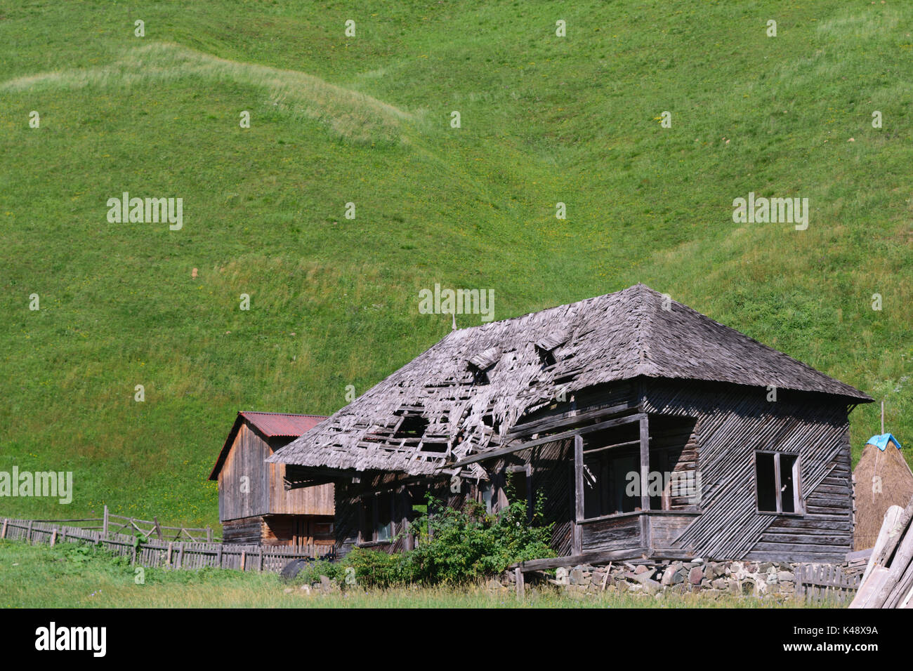 old abandoned wooden house with green grass hills in the background ...