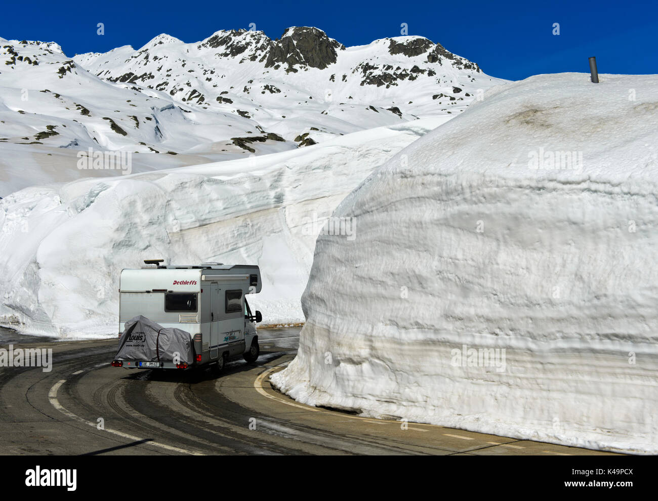 Motorhome Driving On The Pass Road Between High Snow Walls Across The