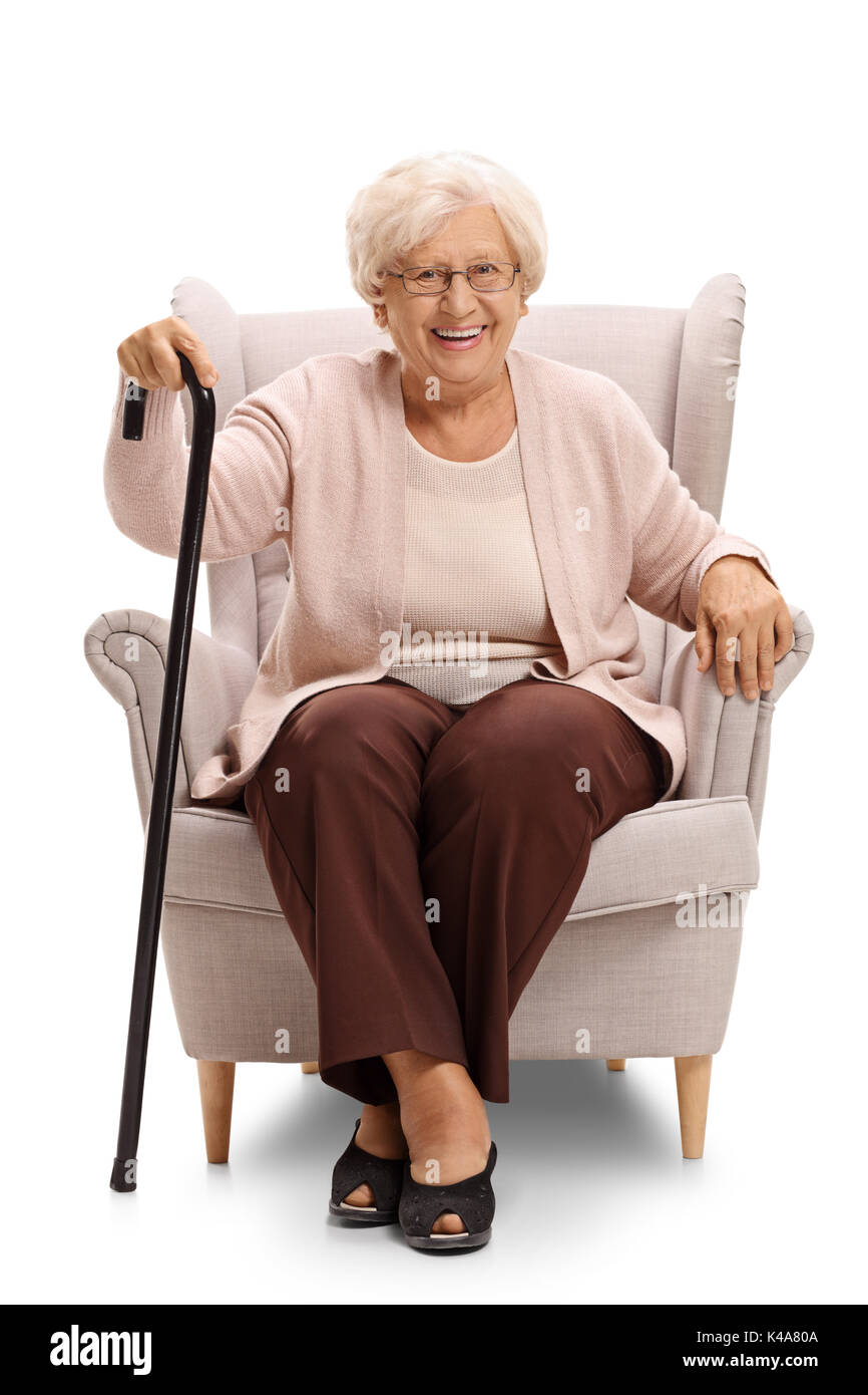 Elderly woman with a cane sitting in an armchair and looking at the camera isolated on white background Stock Photo