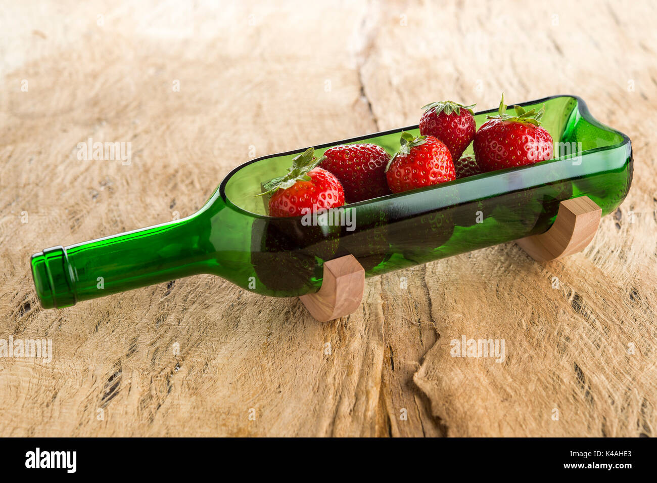 Bottles recycled, sliced open wine bottle on wooden stand, green, decorated with strawberries, on brown wooden plate Stock Photo