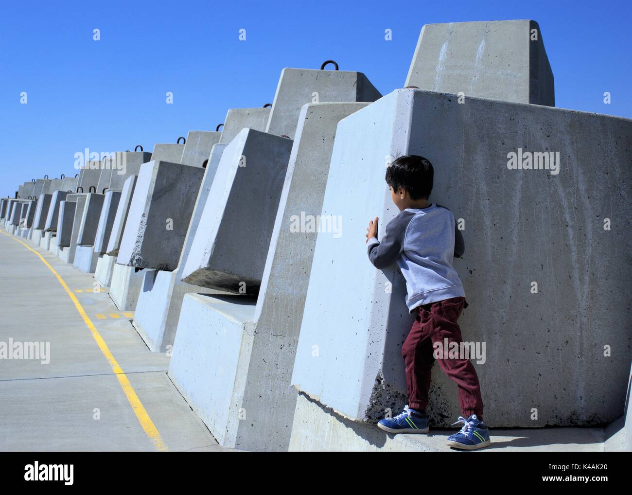 Hide and seek. Boy hiding behind wall, playing hide and seek. Kid peeking out from behind a concrete boulder. Stock Photo