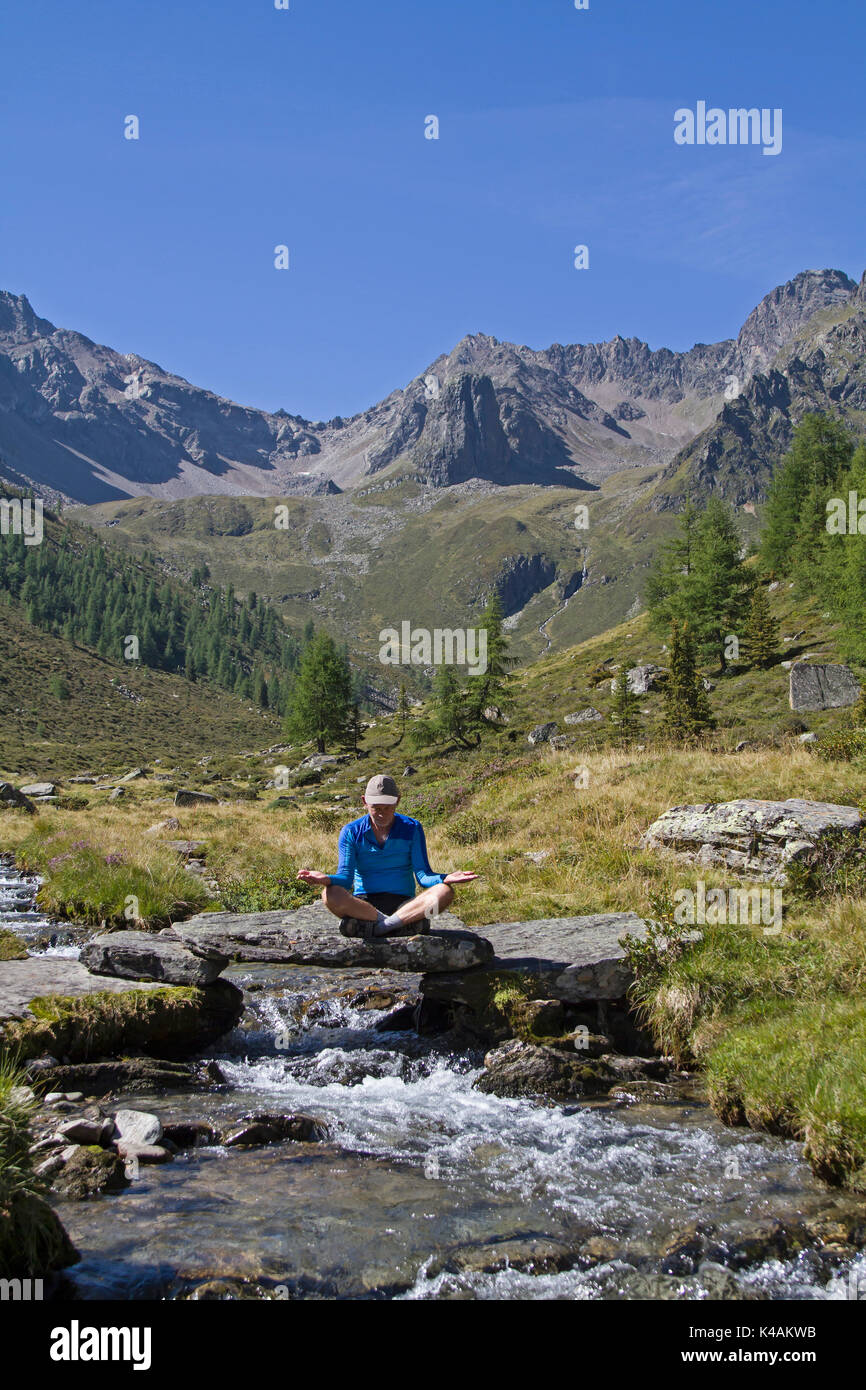 Meditating Man On Small Stone Bridge Over A Wild Stream Stock Photo