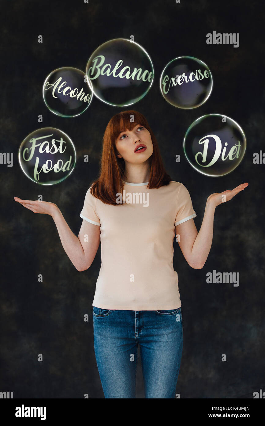 Studio shot of a young woman holding her arms out and looking up while smiling. There are vector bubbles with life-related words in them floating arou Stock Photo