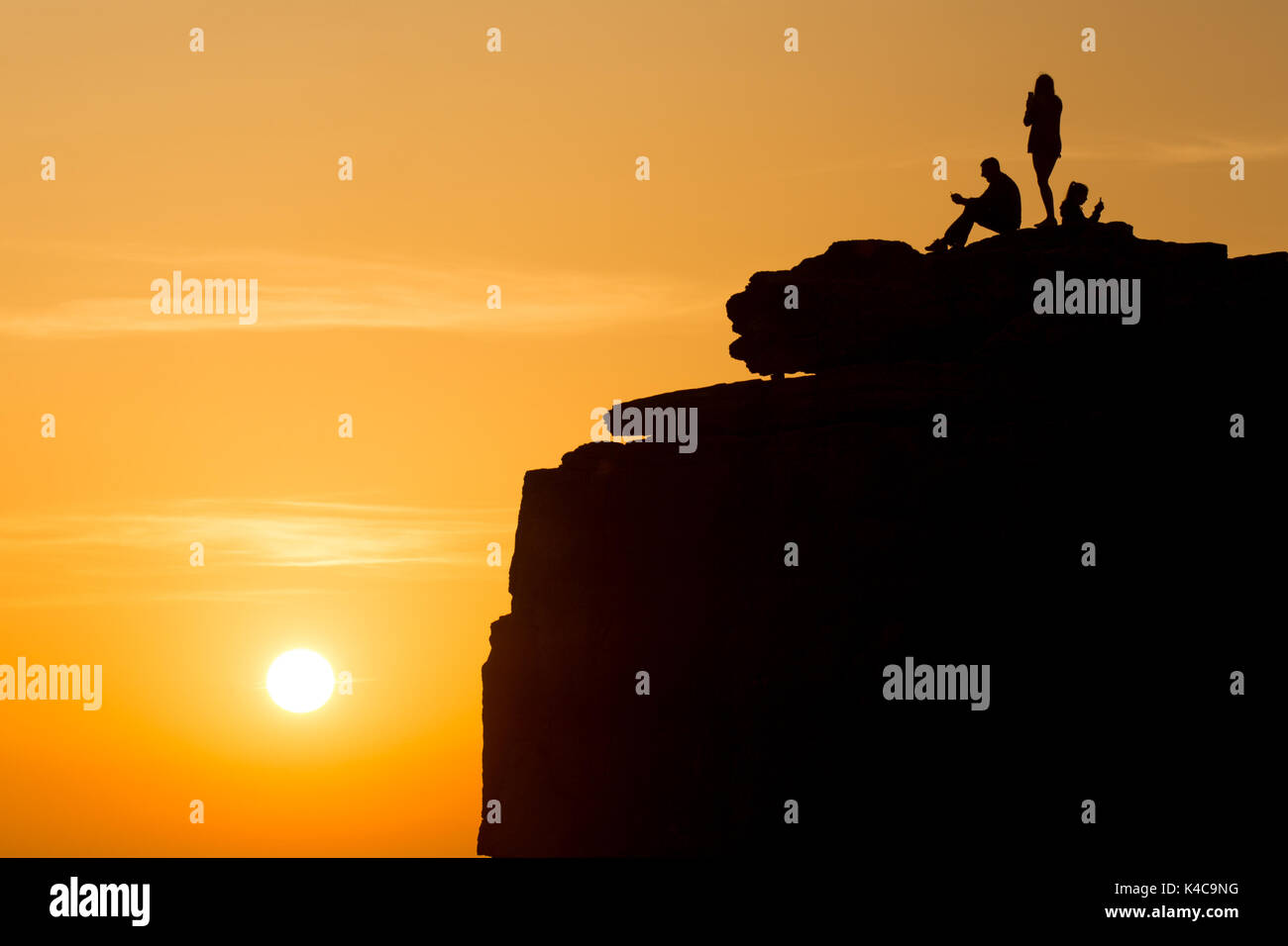 Three people enjoying the sunset on top of a cliff, Pulpit Rock Stock Photo