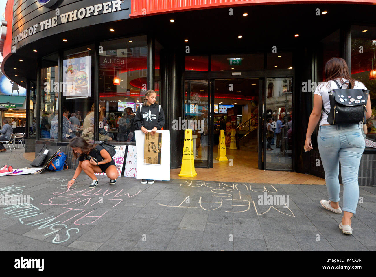 Animal rights activists protesting outside Burger King in Leicester Square, London. Chalking slogans on pavement Stock Photo