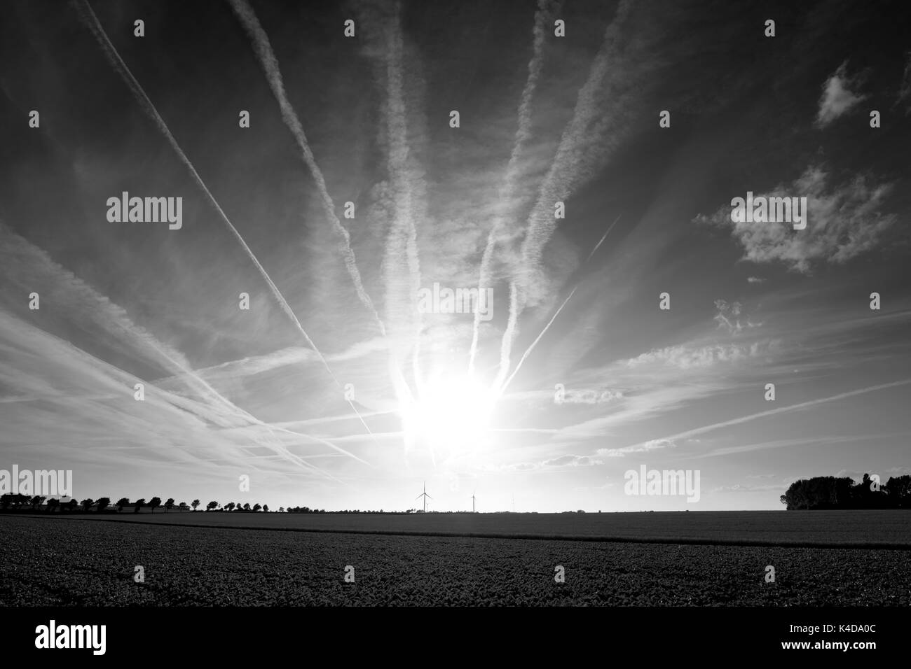 Sunset over agricultural landscape with jet trails leading to the sun. Stock Photo