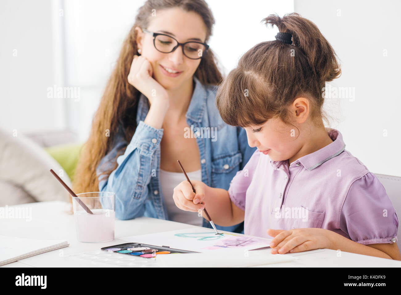 Cute preschool girl painting at home with watercolors, her mother is ...