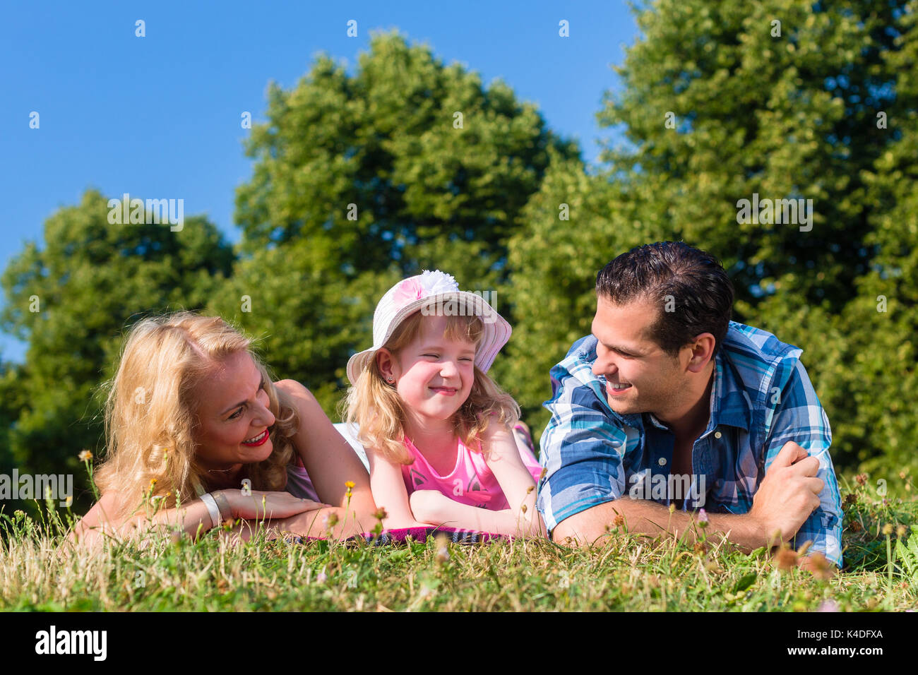 Father, mother, daughter lying on meadow in grass Stock Photo