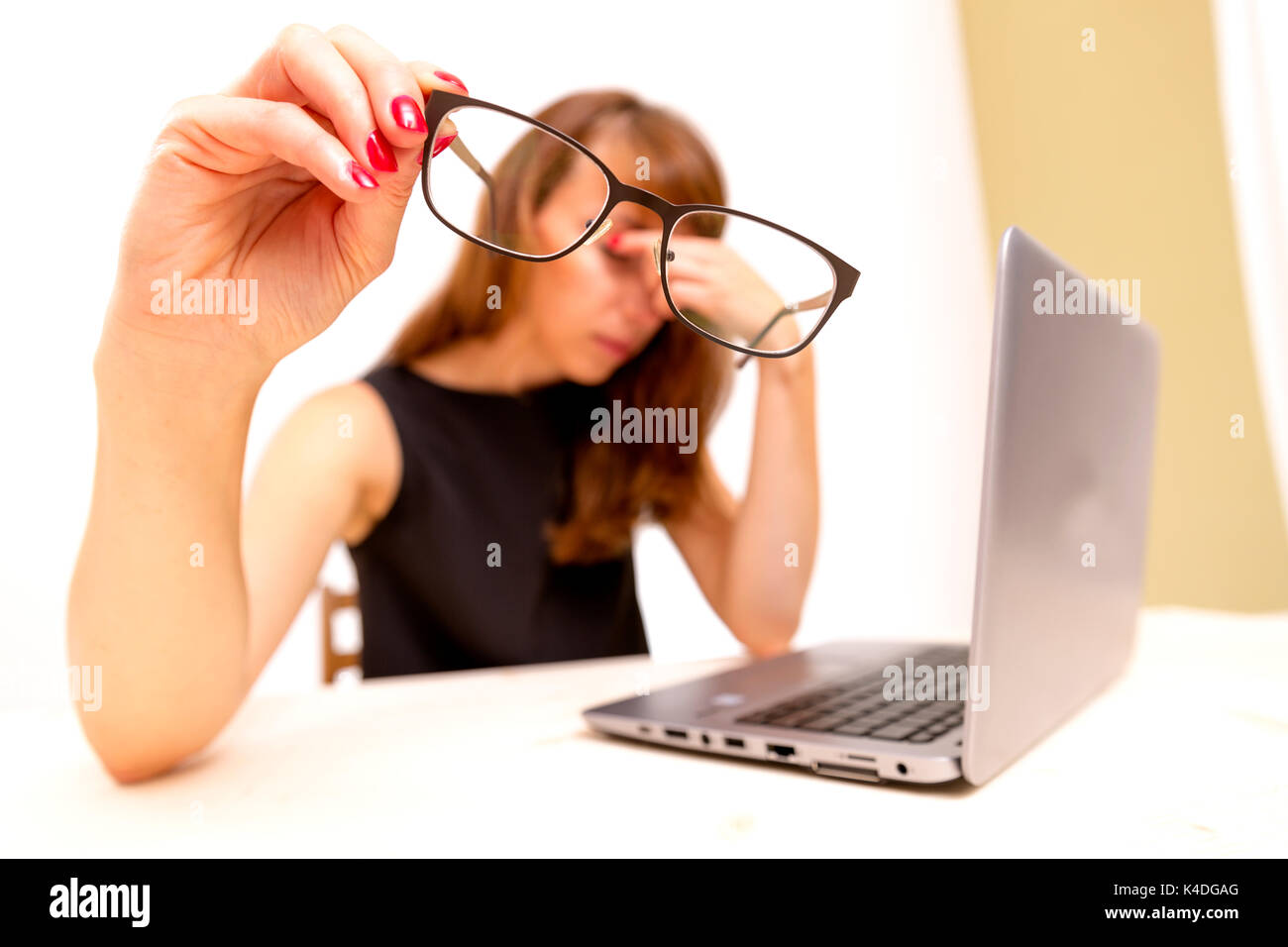 Feeling tired and stressed. Frustrated young woman keeping eyes closed and massaging nose while sitting at her working place in office Stock Photo