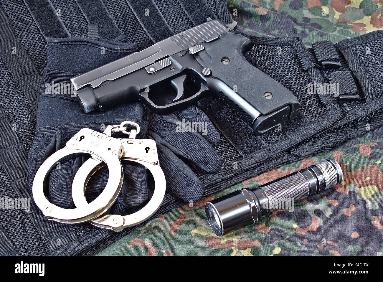 Handgun with handcuffs, gloves and flashlight on black tactical vest and camouflage clothing Stock Photo