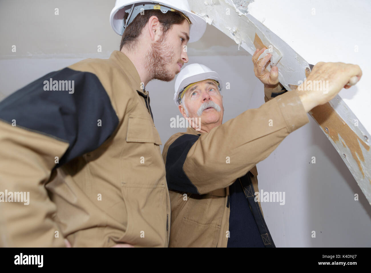Smiling Builders In Hardhat Removing Paint On Wall Indoors Stock